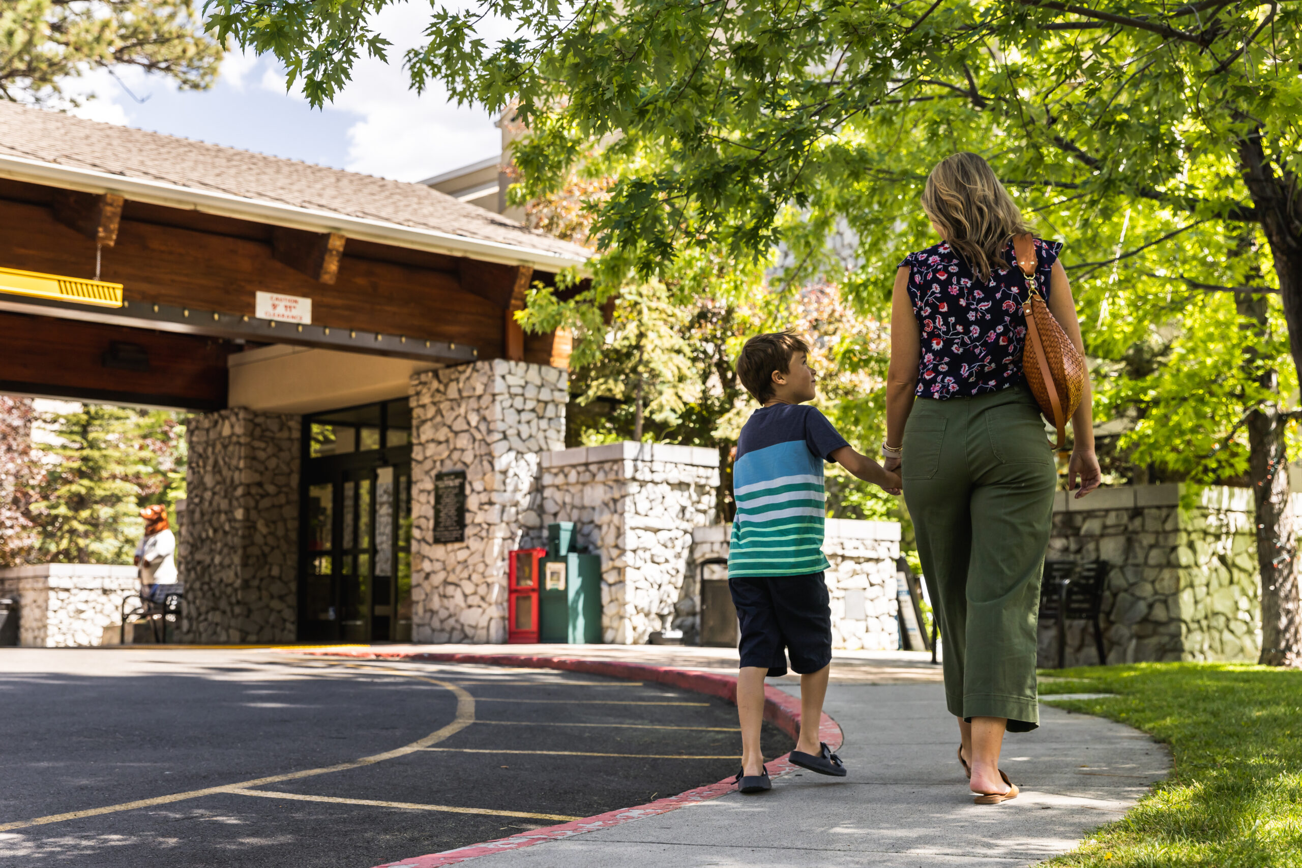 Son holds mothers hand and smiles at her as they walk into a building