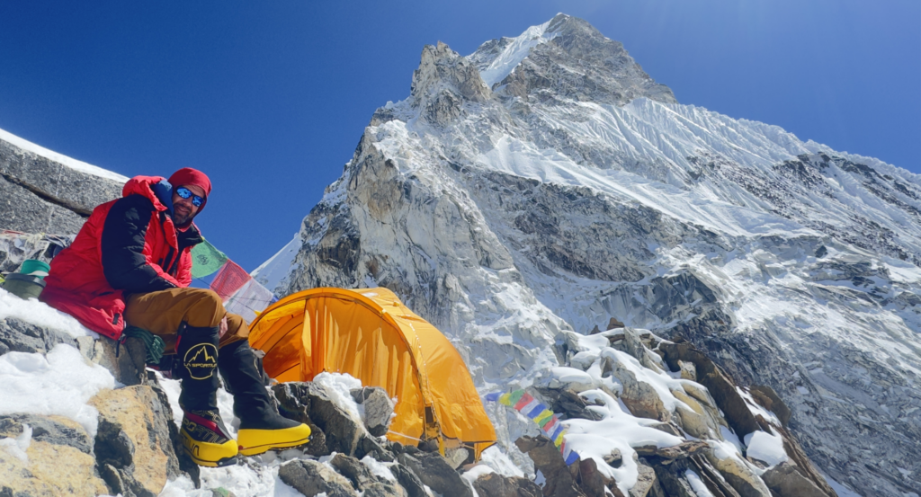 Dr. Habicht sits outside a tent with a mountain peak in the background.